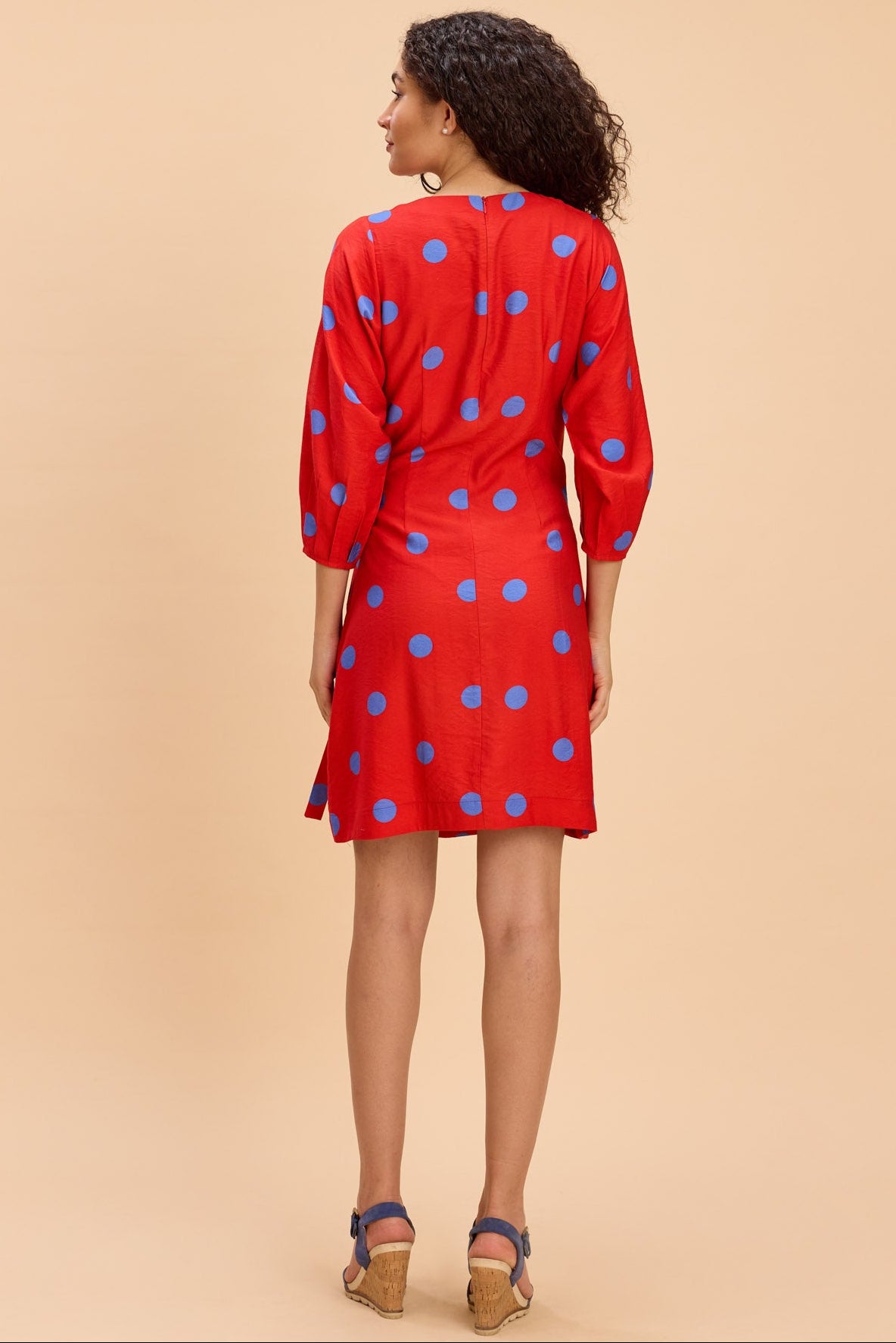 Woman wearing a red dress with blue polka dots on a beige background