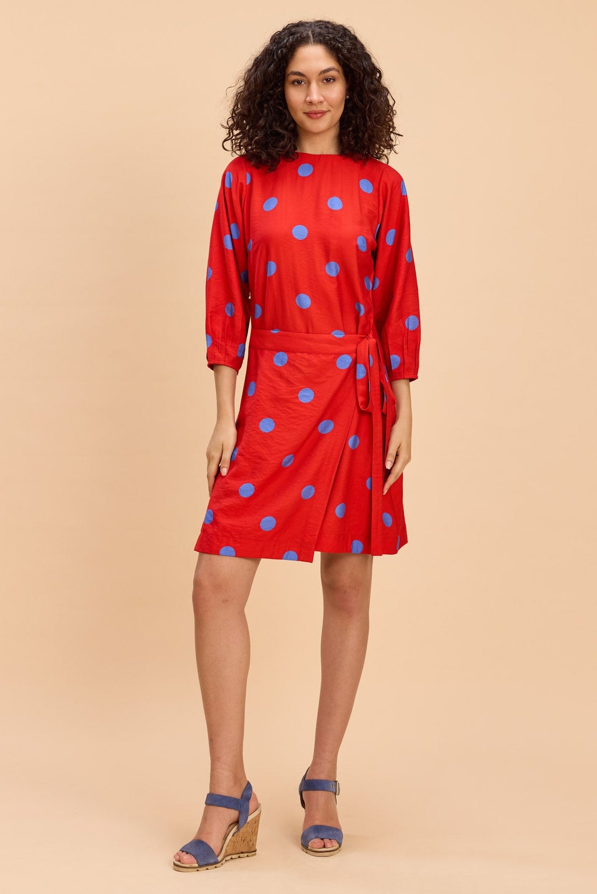 Woman wearing a red dress with blue polka dots against a beige background