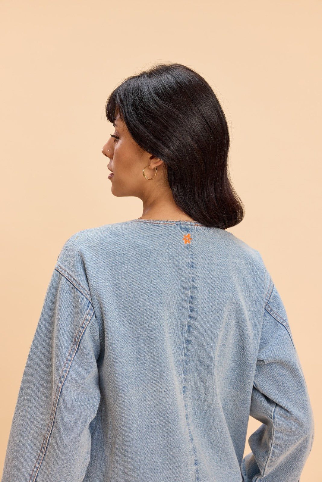 Person wearing a light blue denim jacket on a beige background