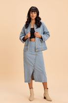 Woman wearing a denim jacket, skirt, and boots on a beige background