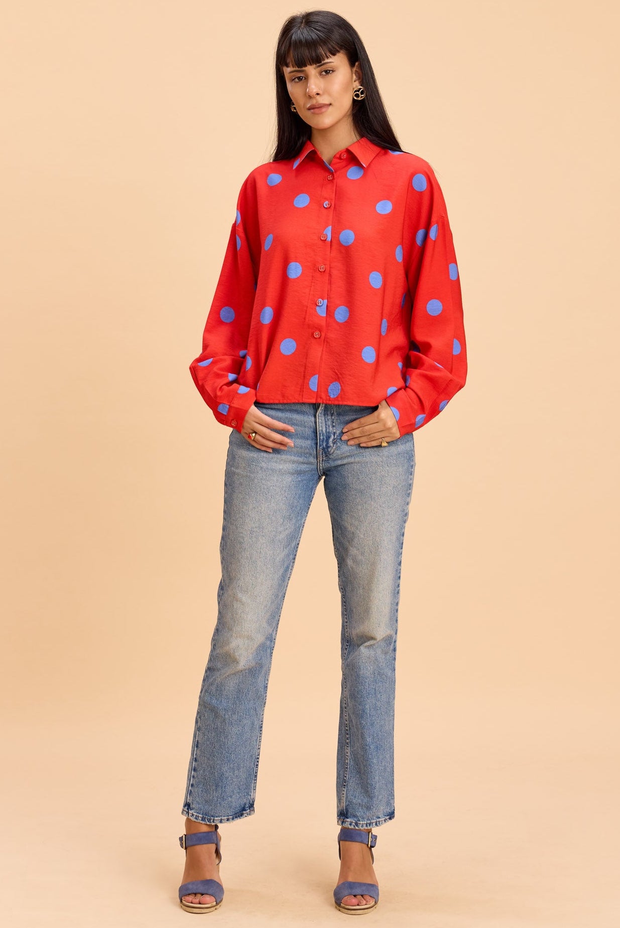 Person wearing a red polka dot shirt and blue jeans on a beige background